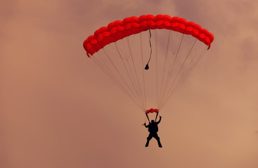 Male parachutist makes the jump from the plane on a red parachute.