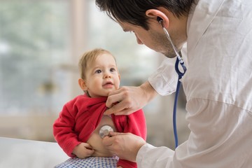 Pediatrician doctor is examining ill child with stethoscope.