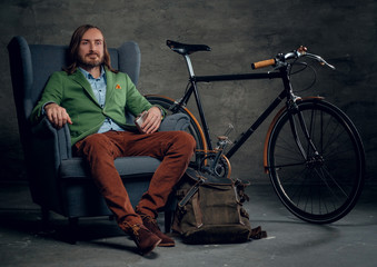 Obraz premium A man sits on a chair with bicycle on background.