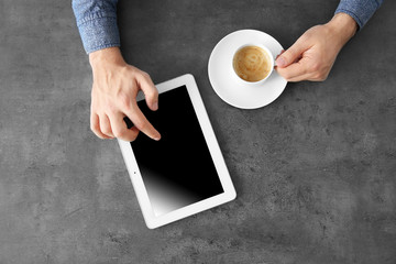 Hands of man sitting at table with tablet computer and cup of coffee