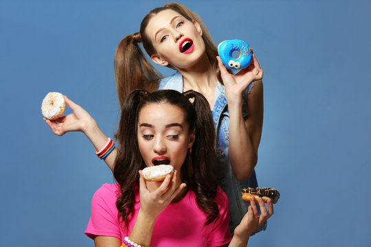 Funny young women with tasty donuts on color background