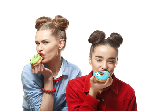 Funny young women eating tasty donuts on white background