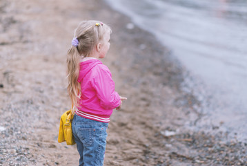 Little girl at rocky beach looking to the sea. Shallow depth of field.