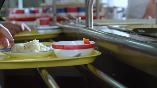 child in canteen takes meat cutlet and puts on plate with rice
