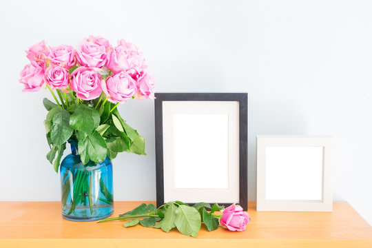 Violet fresh roses with two empty photo frames on wooden shelf