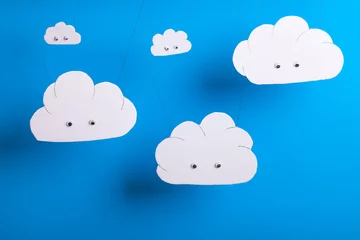 Foto op Canvas Cloud computing concept with white cardboard cutout cute clouds with eyes hanging infront of a sky blue background.  © mreco