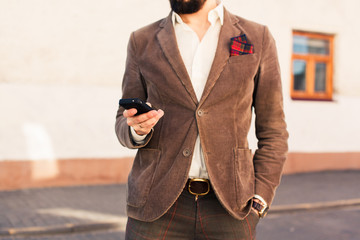 young hipster guy holding a smartphone responds to mail texting and send pictures while sitting on...