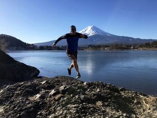 Man running on rocky lake shoreline with snow capped Mt Fuji behind