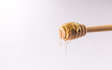 Honey dripping from a wooden honey dipper isolated on white