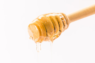 Honey dripping from a wooden honey dipper isolated on white