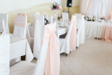 Fototapeta na wymiar White bows made of light pink cloth put on chairs in restaurant