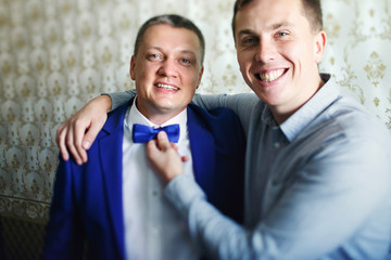 Happy man hugs groom touching a bow tie on his neck