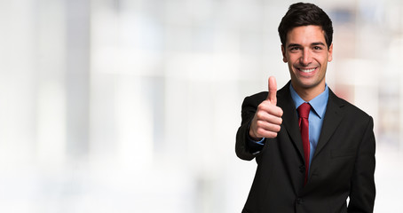 Fototapeta premium Businessman giving thumbs up. Large bright blurred copy-space