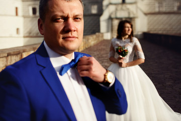 Groom fixes his blue bow tie standing before the bride on old st