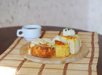 Cheese plate and a cup of coffee. Assorted pickled cheeses on round wooden board on the mat