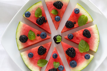 Sliced watermelon pizza with blueberries, blackberries and mint leaf, above view on white.