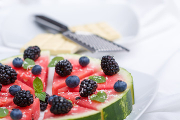Sliced watermelon pizza with blueberries, blackberries , mint leaf and white chocolate crisps, above view.