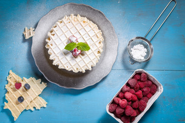 Belgian lush round waffles with fresh raspberries, twigs and leaves minty in plate.