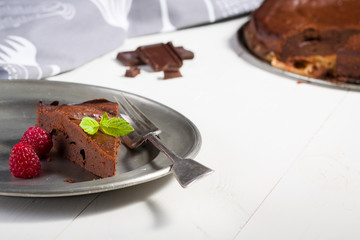 Chocolate brownie with raspberries and leaf of mint, piece lay on plate with fork, at the background is round pie.