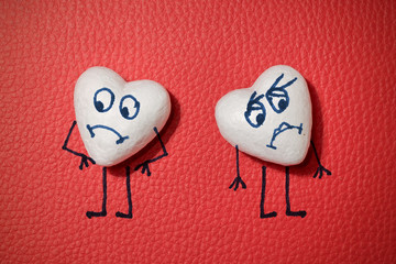 Two white hearts with sad faces on red leather background
