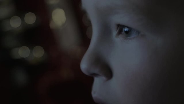 Close-up shot of boy face in the darkness with TV screen reflection in the eyes