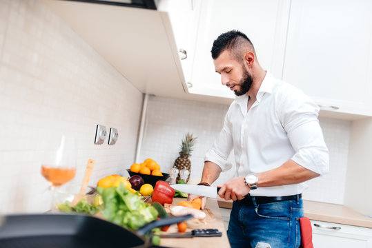 Classy man with elegant shirt cooking dinner for girlfriend. Close up of kitchen cook cutting vegetables and preparing salad