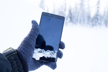 Hand in wool gloved holds smartphone on the background of the winter forest