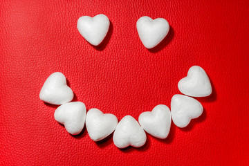 Obraz premium Happy face made from white hearts on red leather background