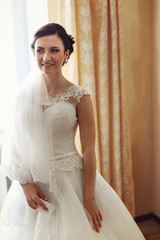 Gorgeous bride in rich dress stands in beige room