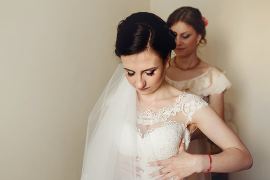 Brunette bride looks down while bridesmaid adjusts her corset