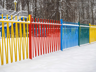Colored metal fence in a park in the snow.
