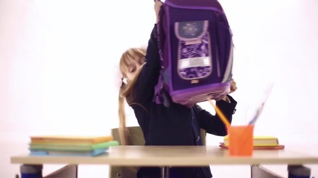 Schoolgirl with a huge backpack sitting at a school desk, she can hardly lift backpack, she puts the textbooks in a backpack
