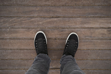 Top view on traveller legs stand on wooden reeks on empty beach, weared blank black sneakers and gray jeans