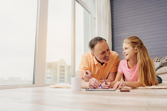 Joyful grandparent and girl drawing picture at home