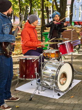 Festival music band. Friends playing on percussion instruments in city park. Girl with blue hair. Fountain and trees in the background.