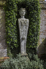 Fototapeta na wymiar Garden wall statue framed by ivy and brachyglottis plants
