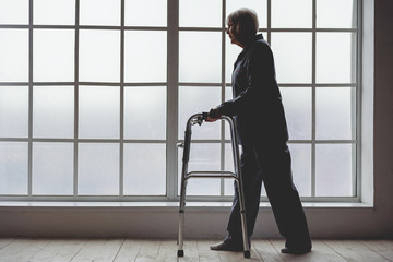 Calm old woman holding foldable walker in room of clinic
