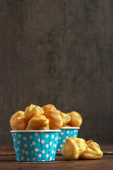 Eclairs or profiterole in blue paper cup on dark background. French dessert. Empty space for design text template.