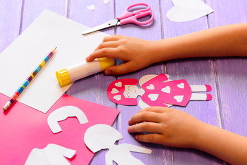 Small child made an angel doll of cardboard. Childrens hands on a wooden table. Craft supplies for...