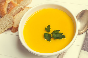 Un cuenco de cerámica blanco con sopa crema de calabaza zapallo junto a una cuchara y unas rodajas...
