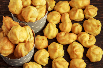 Sweet tasty eclairs or profiterole in gray paper cups with stars on wooden background. French dessert. Empty space for design text template.