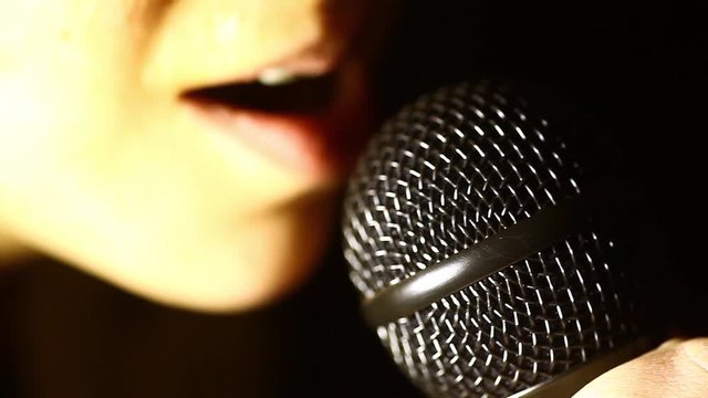 Close up footage of a woman singing to a microphone.