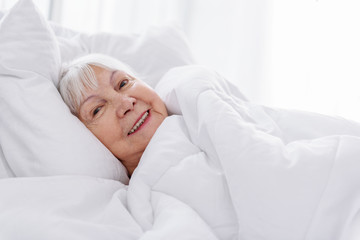 Cheerful retiree wrapping in white soft blanket