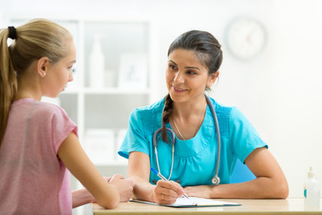 Obraz premium Young woman doctor talking to her teenager patient and writing down the symptoms. Concept of visit to gynecologist