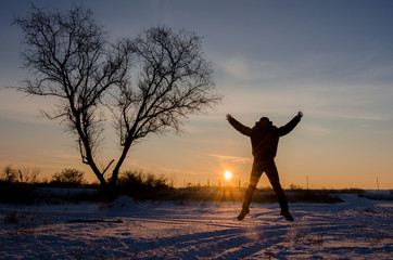 Tree in snow scene with dramatic sunset and jumping man hands up