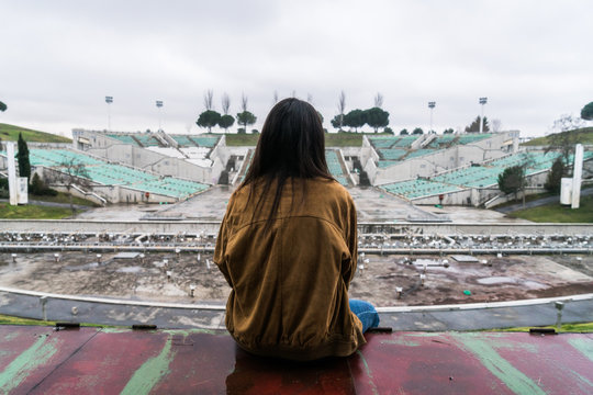 Girl sitting backwards looking at an abandoned stadium