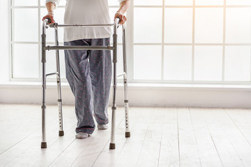 Old woman holding foldable walker and moving in hospital