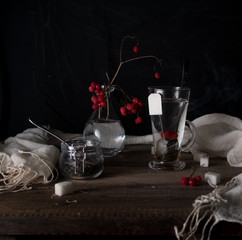 rustic still life. branch viburnum, tea in a big circle and jars on a wooden table. black background