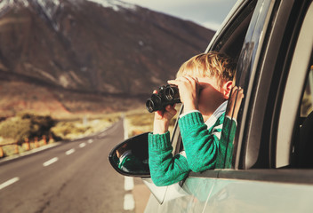 little boy looking through binoculars while travel by car on road
