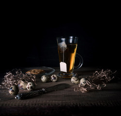 rustic still life. cup of tea and quail eggs on a wooden table. black background